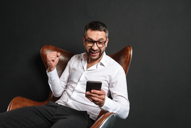 Hombre de negocios emocionado que se sienta usando el teléfono móvil.