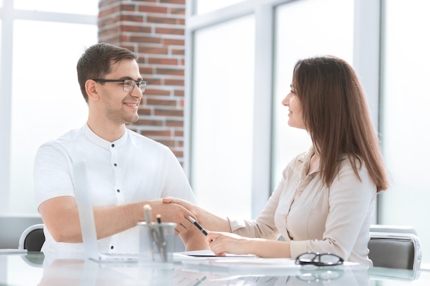 Hombre de negocios y empresaria dándose la mano mientras está sentado en el escritorio. concepto de cooperación