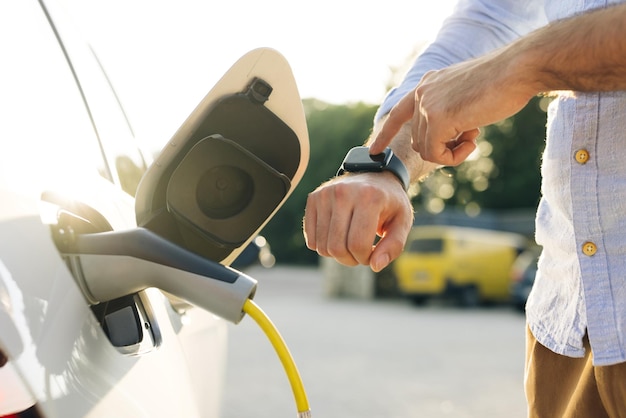 El hombre de negocios enchufando el cable de carga al vehículo eléctrico, la mano masculina inserta el conector de alimentación