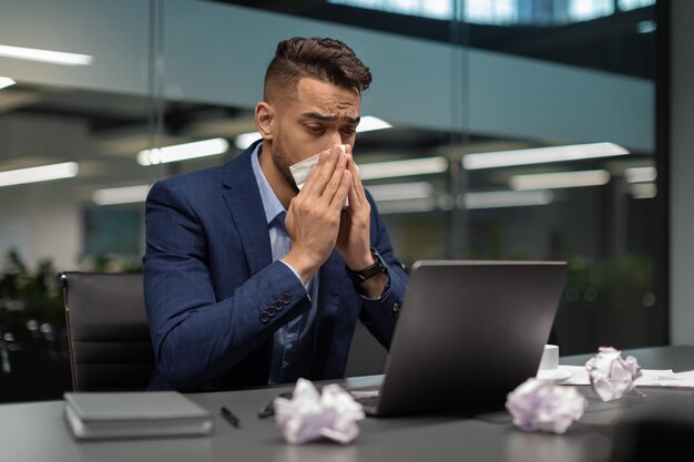 Hombre de negocios enfermo del Medio Oriente sentado en su oficina estornudando