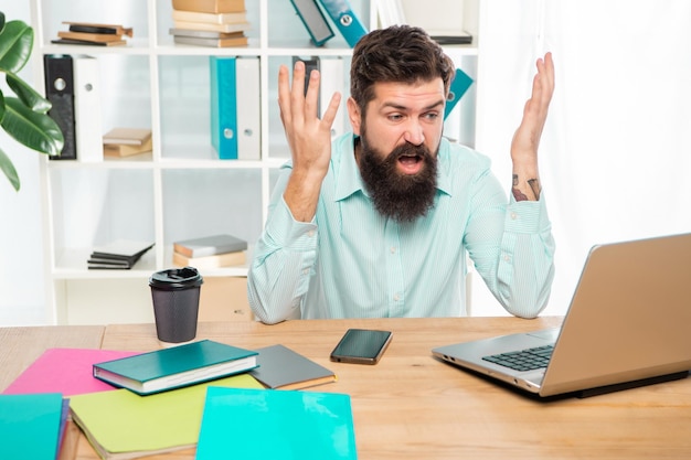 Hombre de negocios enojado que trabaja en la computadora portátil en el trabajo de escritorio de oficina