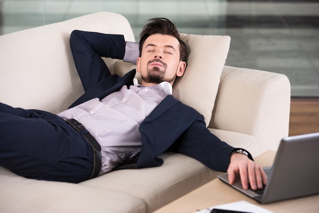 El hombre de negocios está durmiendo en el sofá en la oficina.