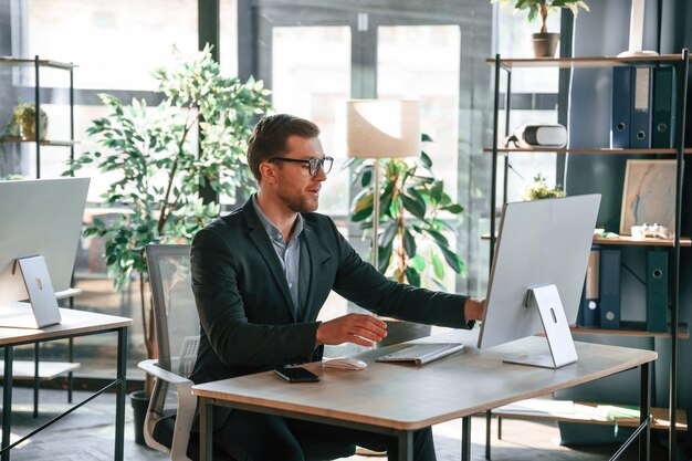 El hombre de negocios está sentado frente a la computadora y trabajando en la oficina.