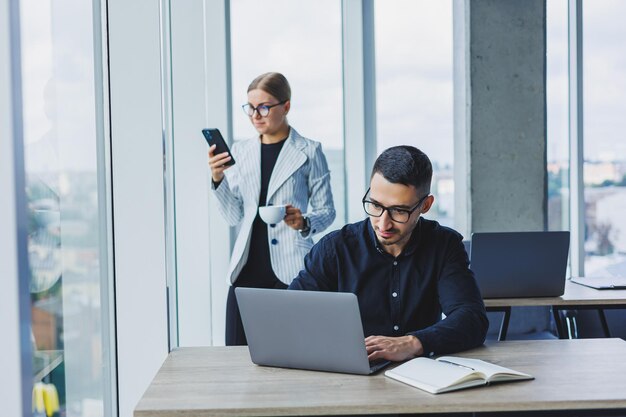 Un hombre de negocios está trabajando en una computadora portátil mientras habla mientras su colega escucha Trabajar en una oficina moderna y luminosa