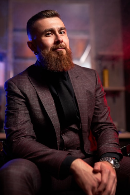 Hombre de negocios con estilo elegante en traje formal se sienta en una habitación oscura