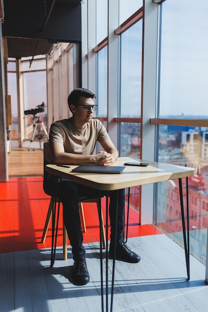 Un hombre de negocios europeo se sienta con una computadora portátil durante el almuerzo en un café El concepto de trabajo remoto e independiente Un hombre adulto exitoso sonriente con anteojos está sentado en una mesa de madera un día soleado