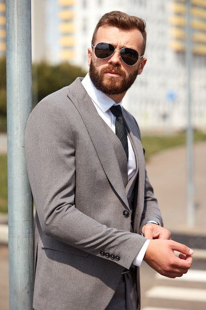 Hombre de negocios exitoso con estilo en traje y gafas de sol arreglar un botón al aire libre