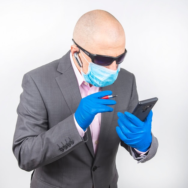 Hombre de negocios exitoso con máscara protectora y guantes trabaja en un teléfono inteligente durante la cuarentena del coronavirus. Trabaja como autónomo en línea.