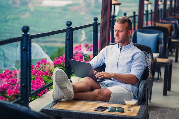 Hombre de negocios exitoso que trabaja de vacaciones detrás de una computadora portátil con vista a la montaña Flujo de trabajo del administrador en línea Trabaja al aire libre con una hermosa vista desde el balcón