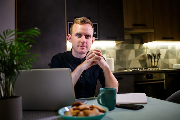 Hombre de negocios exitoso sentado en una mesa en casa, mirando la pantalla de una computadora portátil, se siente satisfecho con el orgullo por el trabajo realizado, el hombre sereno trabaja, las manos detrás de la cabeza, el trabajo en casa