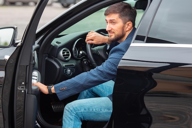 Un hombre de negocios exitoso con un teléfono en la mano se sienta al volante de un automóvil prestigioso