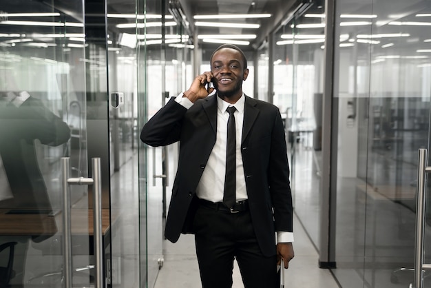 Hombre de negocios exitoso tener conversación telefónica mientras está de pie en el pasillo de la oficina vacía. Hombre banquero profesional en traje hablando por teléfono móvil durante las vacaciones de trabajo.