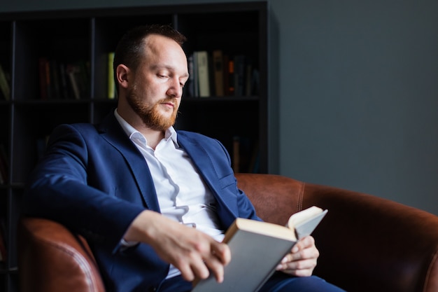 Hombre de negocios exitoso en un traje se sienta leyendo un libro.