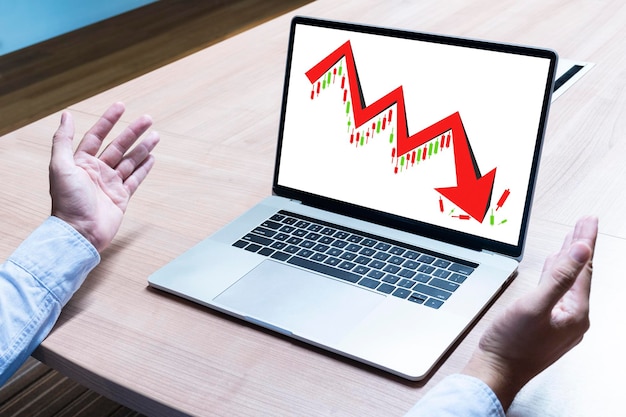 El hombre de negocios extendió sus manos con el gráfico de acciones de tendencia bajista de flecha roja en la pantalla del portátil