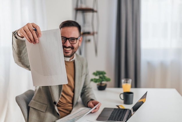 Hombre de negocios feliz analizando informes mientras trabaja en una computadora portátil en la oficina corporativa