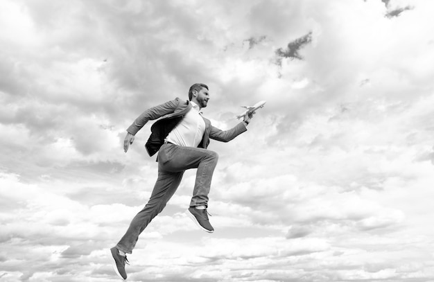 Un hombre de negocios feliz con chaqueta sostiene un avión de juguete en el fondo del cielo para lograr el éxito