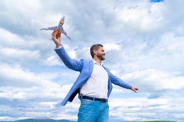 Hombre de negocios feliz confiado en chaqueta mantenga avión de juguete sobre fondo de cielo, éxito empresarial