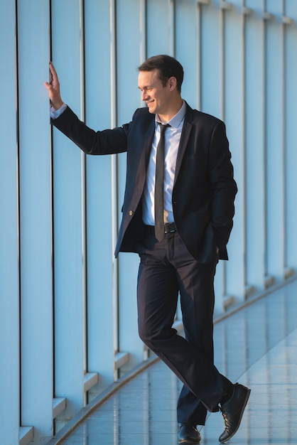 El hombre de negocios feliz está parado cerca de la ventana panorámica