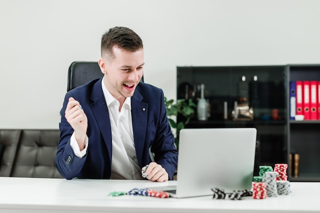 Hombre de negocios feliz gana en el casino en línea mientras juega póker en la oficina en el lugar de trabajo