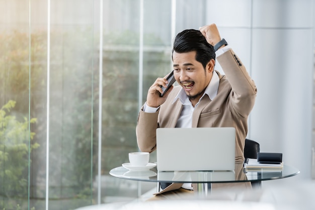 Hombre de negocios feliz hablando por teléfono móvil y usando laptop