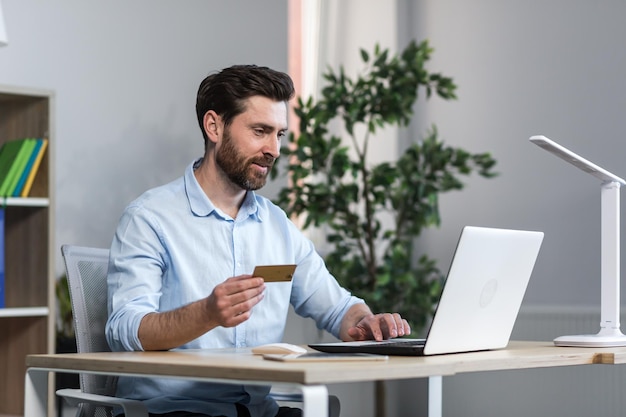 Un hombre de negocios feliz hace compras en línea trabajando en la oficina, el esposo tiene una tarjeta de crédito y usa una computadora portátil