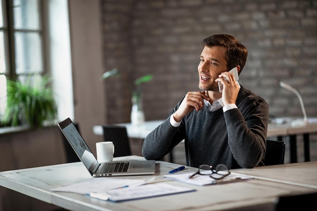 Hombre de negocios feliz haciendo una llamada telefónica en el teléfono móvil mientras trabaja en la oficina