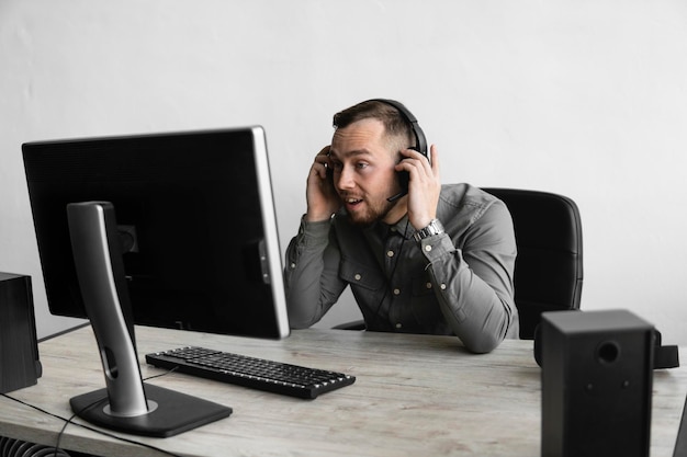 Hombre de negocios feliz impresionado en una camisa que se sienta contra el monitor de la computadora en auriculares