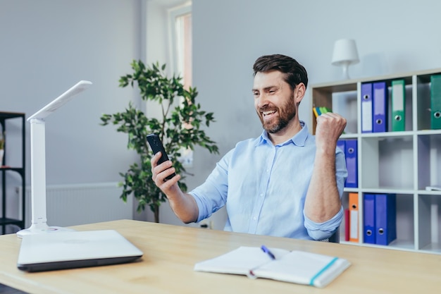 Foto hombre de negocios feliz leyendo buenas noticias del hombre del teléfono que trabaja en la oficina