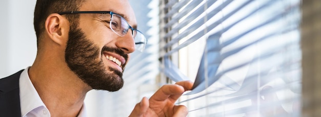 El hombre de negocios feliz mirando a través de las persianas