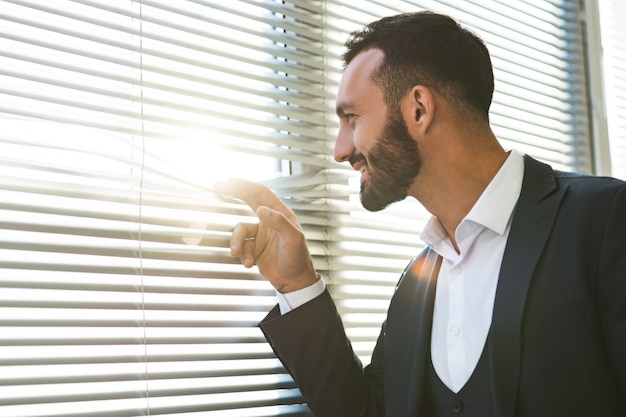 El hombre de negocios feliz mirando a través de las persianas