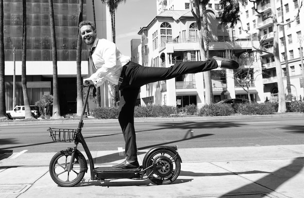 Hombre de negocios feliz montando scooter eléctrico en transporte de alquiler de fondo de paisaje urbano