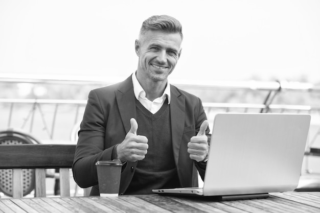 Un hombre de negocios feliz muestra los pulgares haciendo un gesto de aprobación trabajando en una computadora portátil fuera de los pulgares