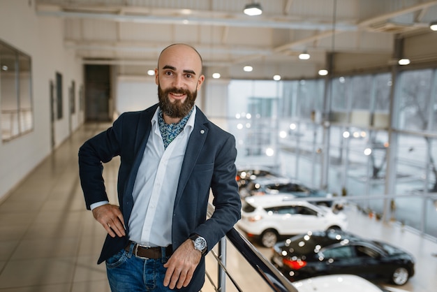 Foto hombre de negocios feliz posa en concesionario de automóviles. cliente en la sala de exposición de vehículos nuevos, persona del sexo masculino que compra un automóvil, negocio de concesionario de automóviles