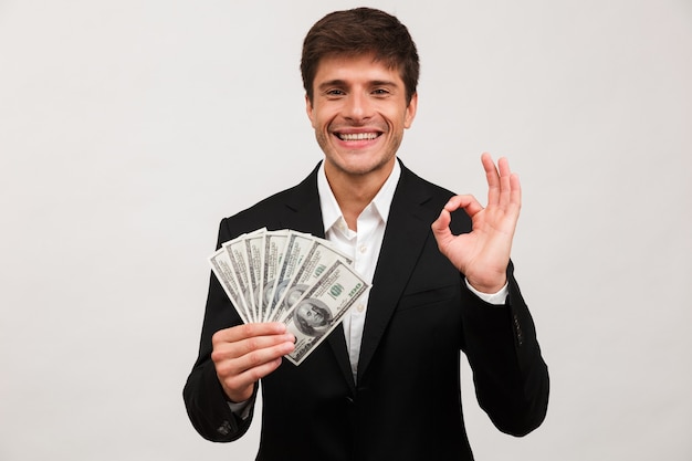 El hombre de negocios feliz que se coloca aislado que sostiene el dinero hace un gesto bien.