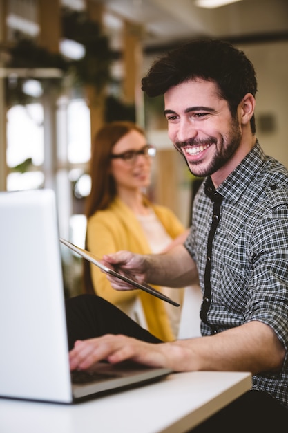 Hombre de negocios feliz que usa la computadora portátil con el compañero de trabajo femenino