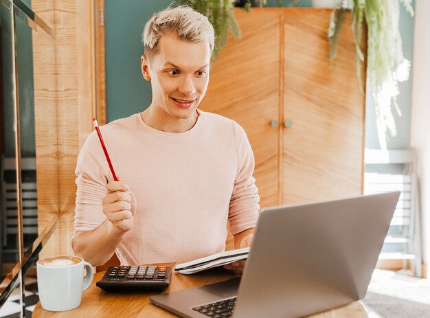 Hombre de negocios feliz sentado en la cafetería con ordenador portátil y smartphone. Hombre de negocios enviando mensajes de texto en un teléfono inteligente mientras está sentado en un café, trabajando y revisando el correo electrónico en la computadora