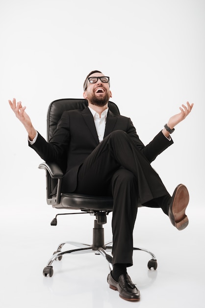 Hombre de negocios feliz sobre la pared blanca que se sienta en silla.