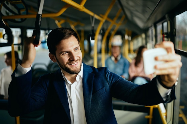 Hombre de negocios feliz tomando selfie mientras viaja al trabajo en autobús