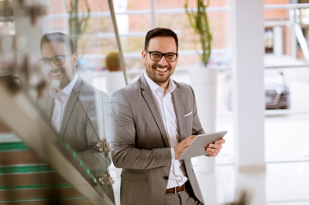 El hombre de negocios feliz se vistió en el traje que se colocaba en oficina moderna y que usaba la tableta