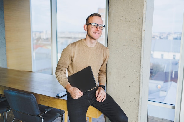 Un hombre de negocios con gafas y ropa elegante bebe café en un espacio de trabajo moderno Un trabajador independiente masculino con una computadora portátil trabaja de forma remota