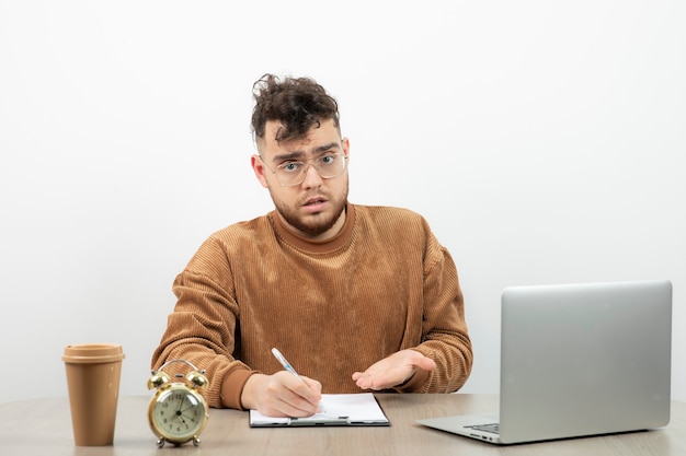 Hombre de negocios con las gafas sentado y usando la computadora portátil en la oficina y tomando notas.