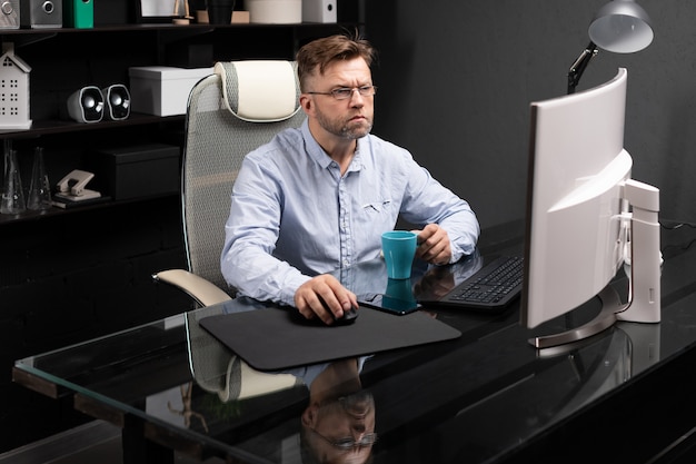Hombre de negocios con gafas trabajando en la oficina en la mesa de la computadora y tomando café de una pequeña taza
