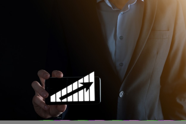 El hombre de negocios con gráficos holográficos y estadísticas del mercado de valores obtiene beneficios. Concepto de planificación del crecimiento y estrategia empresarial. Visualización de pantalla digital de buena forma económica.