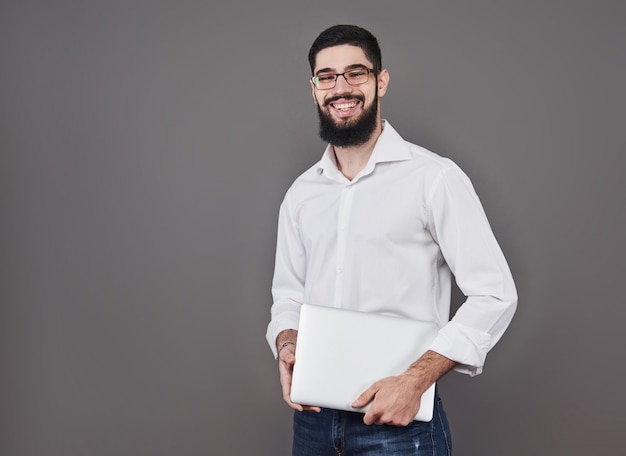 Hombre de negocios guapo en gafas y traje con laptop en manos y escribir algo. Vista lateral. Gris aislado