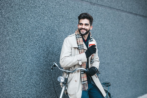 Hombre de negocios guapo joven de pie en las calles de la ciudad con bicicleta. Protección del medio ambiente y concepto de transporte ecológico.