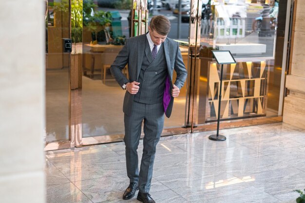 Hombre de negocios guapo en traje formal gris de pie cerca de un edificio moderno y mirando hacia abajo