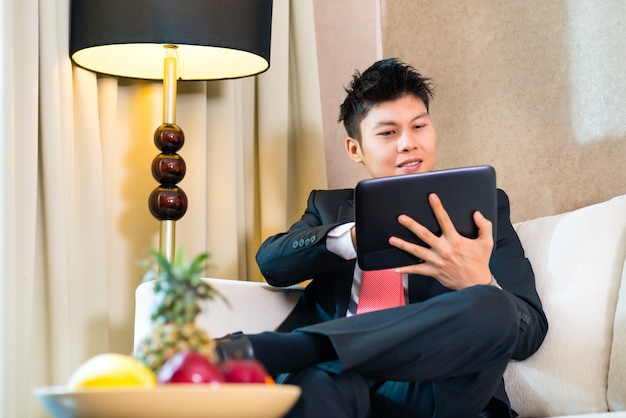 Hombre de negocios en la habitación de hotel asiática que trabaja con la tableta