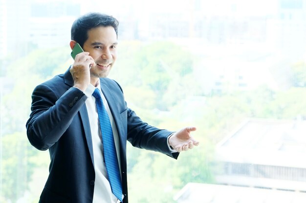 Hombre de negocios hablando teléfono inteligente por windows con vistas a la ciudad