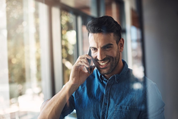 Hombre de negocios hablando por teléfono mientras se ve feliz, sonriente y alegre en una oficina moderna en el trabajo