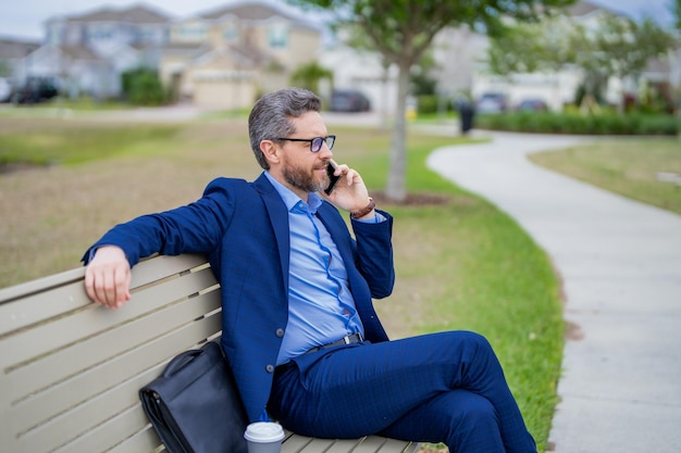 Hombre de negocios hablar por teléfono sentado en un banco en el parque hombre en traje llamar al teléfono fuera guapo busine